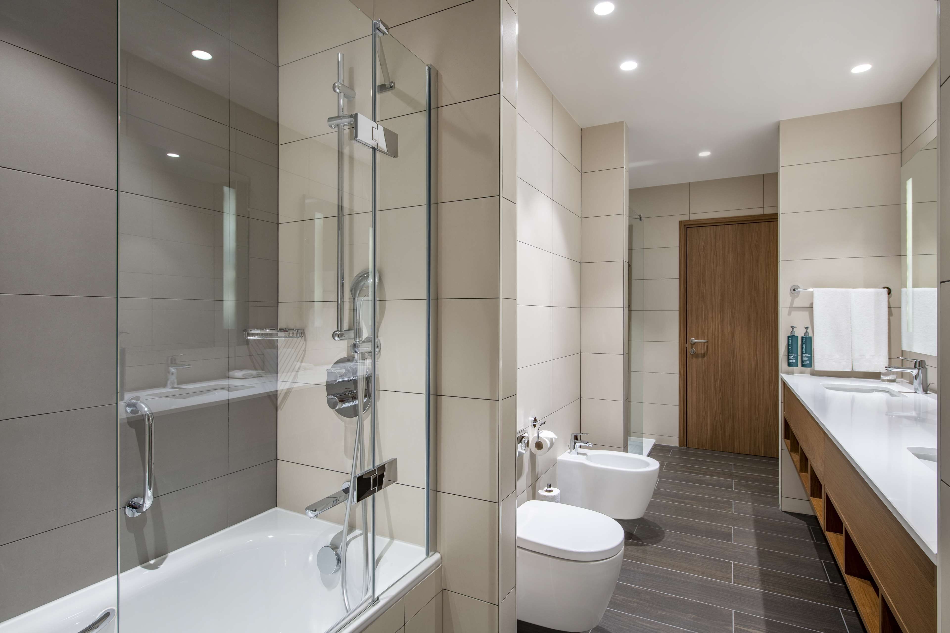 Un baño moderno con ducha envuelta en cristal, bañera independiente, inodoro y tocador con espejo.