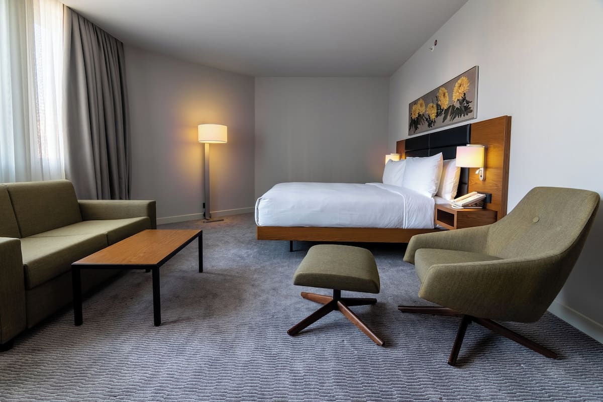 Een hotelkamer met een bed, twee fauteuils, een bank, een salontafel en een vloerlamp.