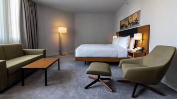 Una habitación de hotel con cama, dos sillones, un sofá, una mesita y una lámpara de pie.