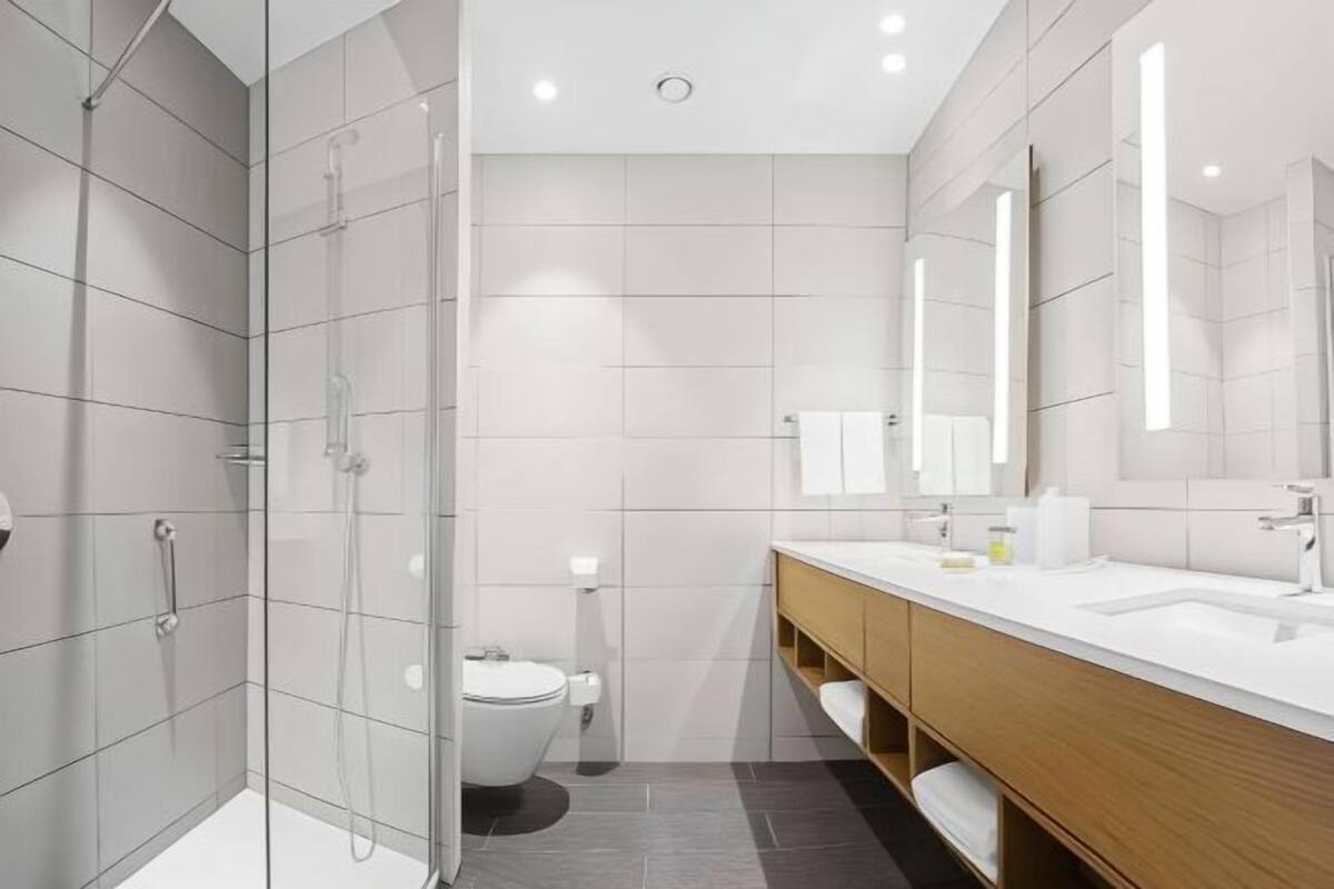 Een moderne badkamer met een glazen douchecabine, toilet en een wastafel met spiegel.