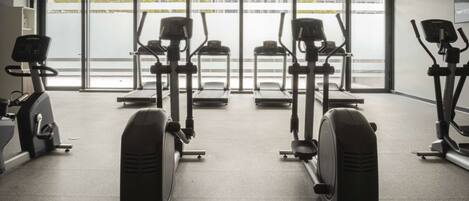 A gym with cardio machines, large windows, and a view of the outside.