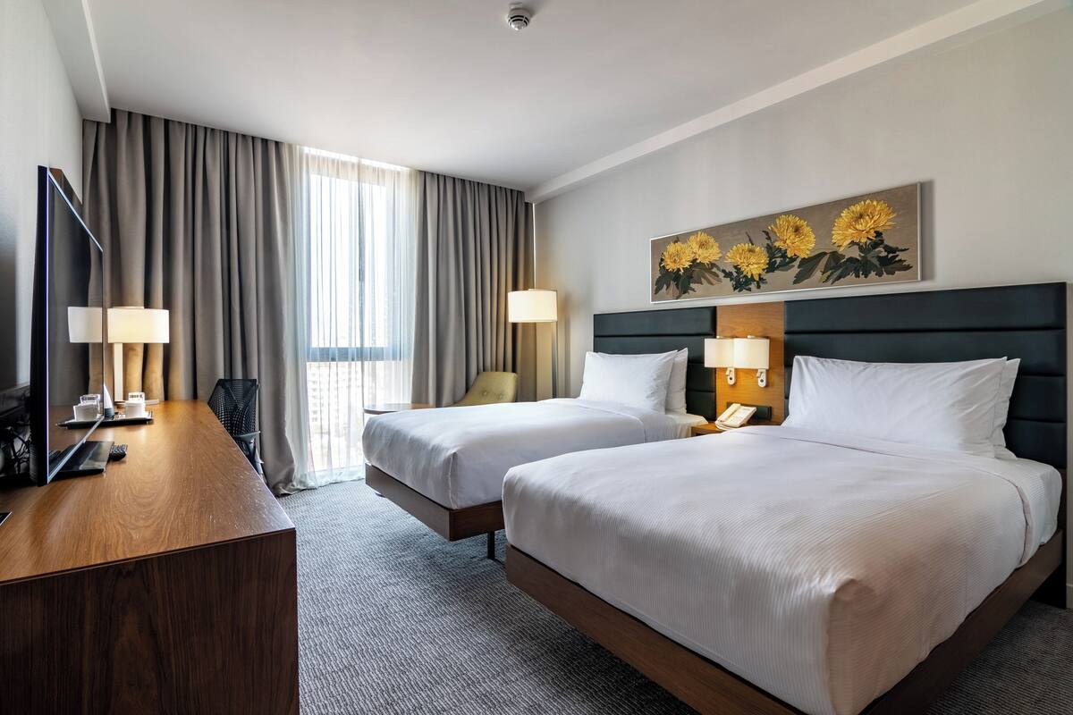 Een hotelkamer met twee bedden, een bureau, een televisie en een schilderij van zonnebloemen.