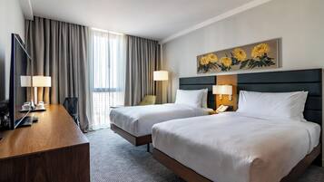 Een hotelkamer met twee bedden, een bureau, een televisie en een schilderij van zonnebloemen.
