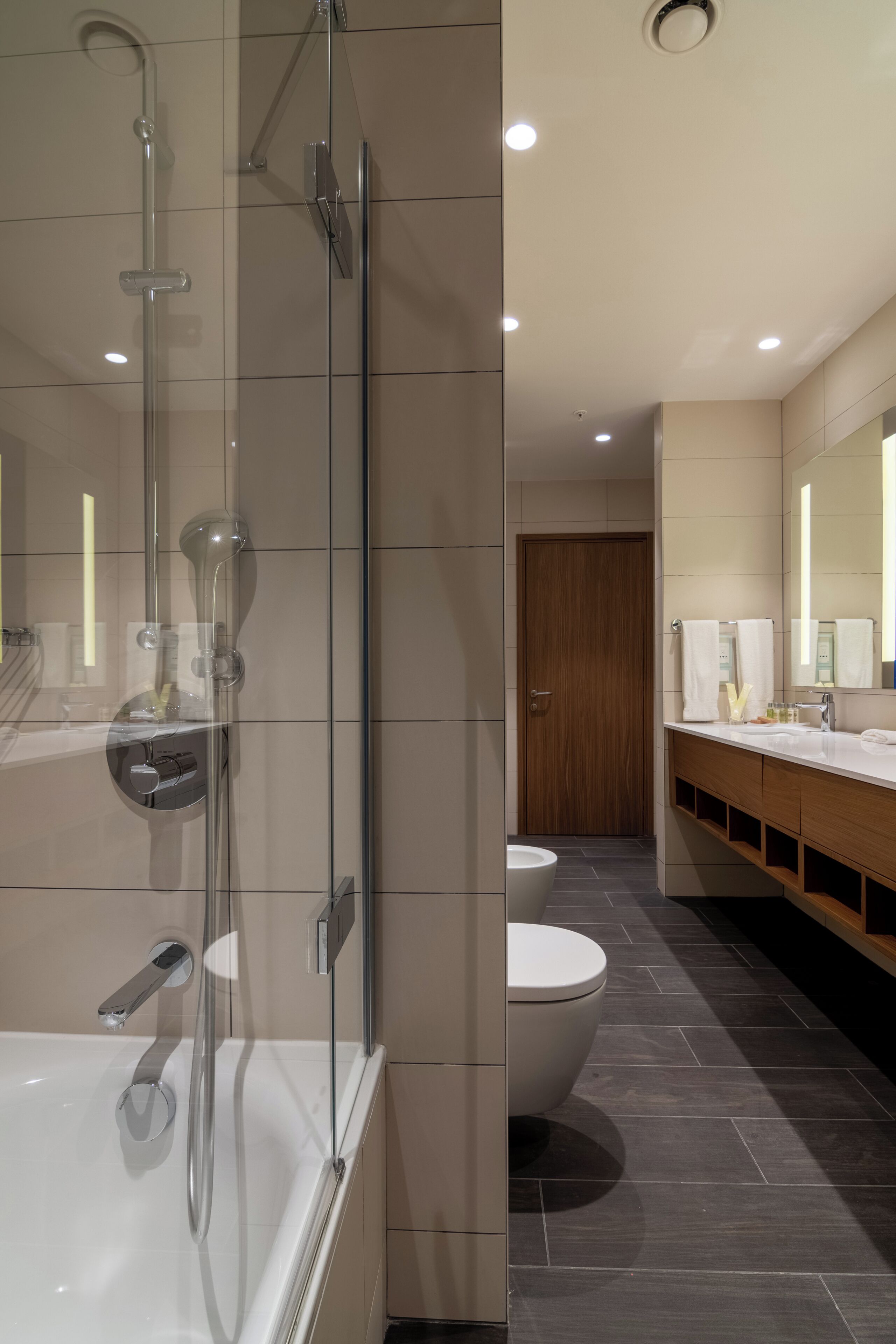 A modern bathroom with a glass-enclosed shower, a white bathtub, a toilet, and a vanity with a mirror.