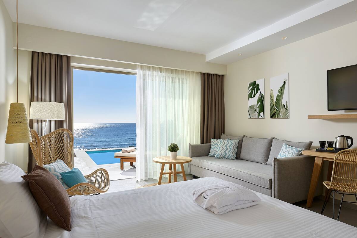 A hotel room with a bed, a sofa, a dining table, and a view of the ocean.