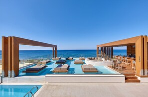 Una piscina a sfioro sul tetto con sedie a sdraio e un'area bar, con vista sull'oceano.