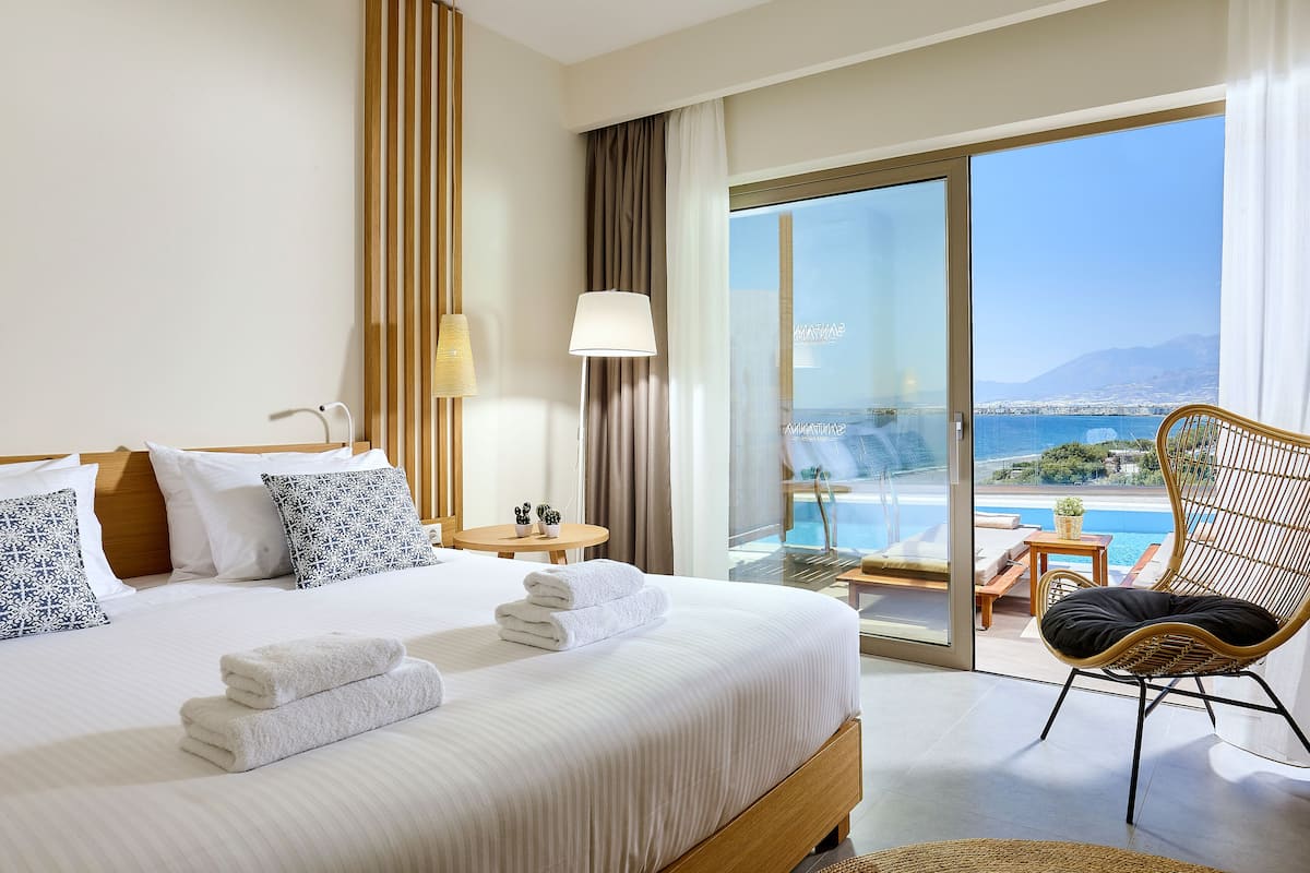 A hotel room with a large bed, a balcony with a view of the sea, and a wicker chair.