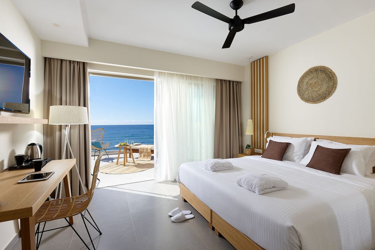 A hotel room with a bed, a desk, a chair, a TV, and a view of the sea.