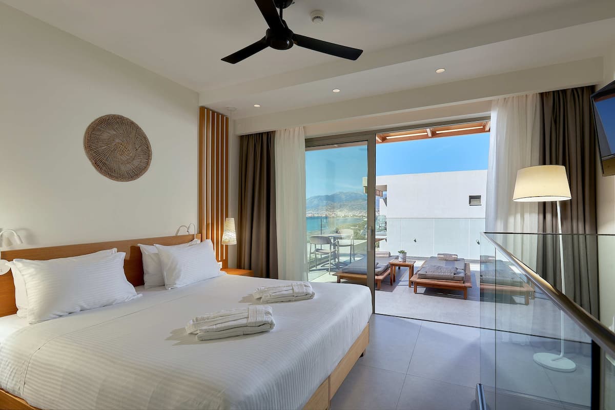 A hotel room with a large bed, a ceiling fan, a TV, and a balcony with a table and chairs.