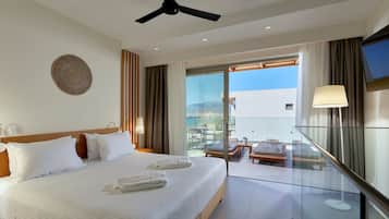 Habitación de hotel con una cama grande, ventilador de techo, televisión y balcón con mesa y sillas.