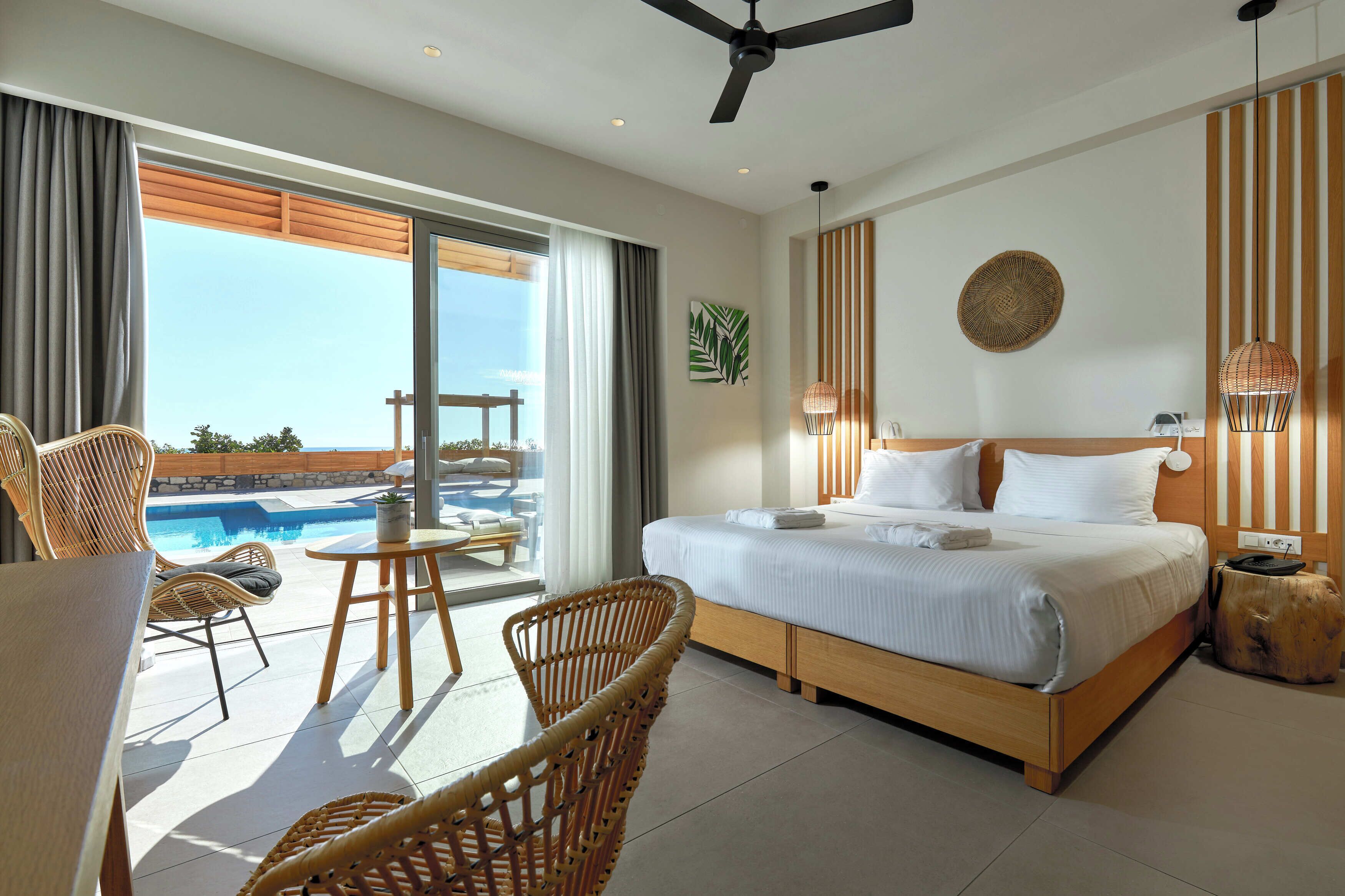 Quarto de hotel com cama, mesa de jantar, cadeiras, ventilador de teto, vista para a piscina e uma janela grande.