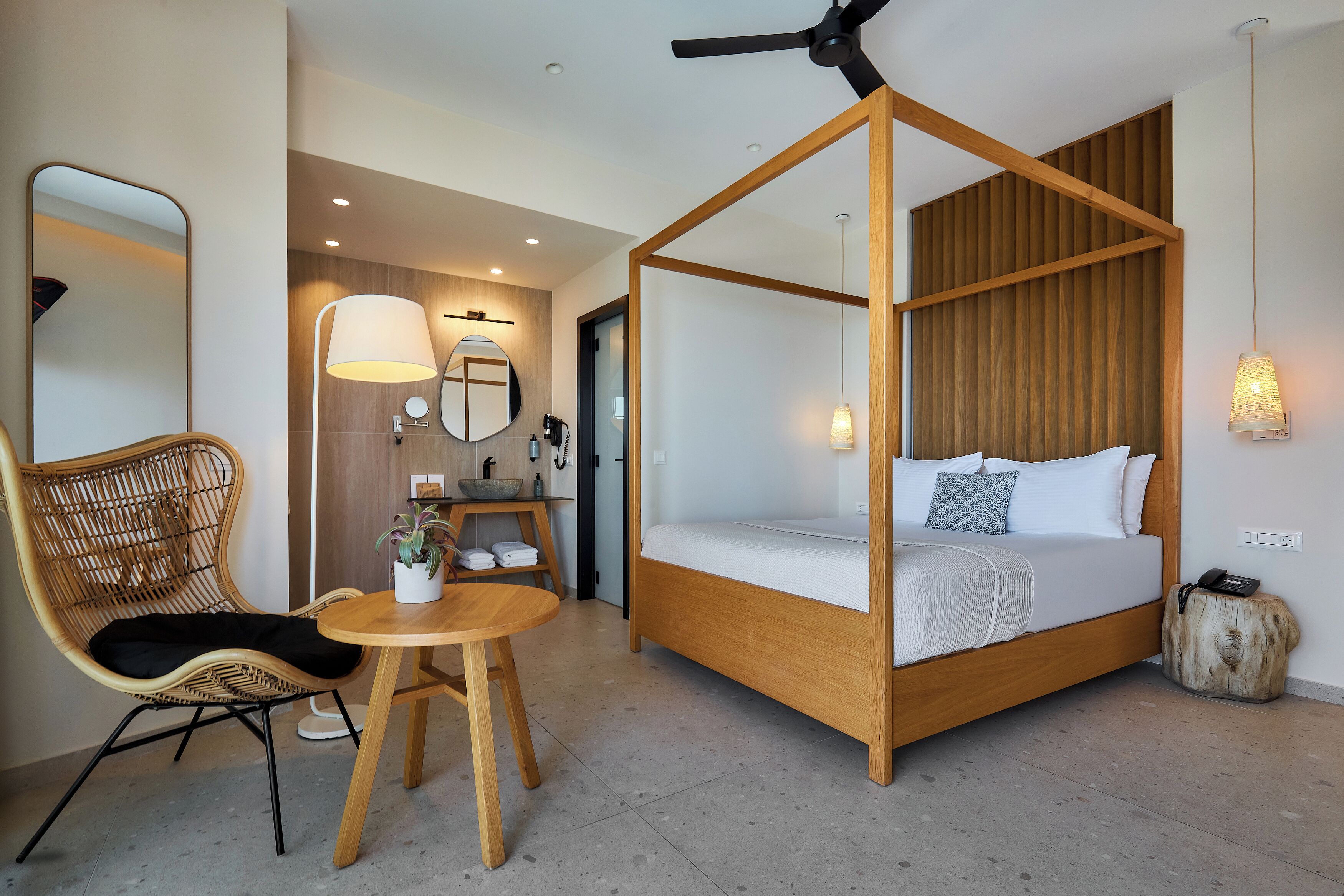 Un dormitorio con una cama con dosel, una mesa redonda de madera, una silla de mimbre y una lámpara de noche.