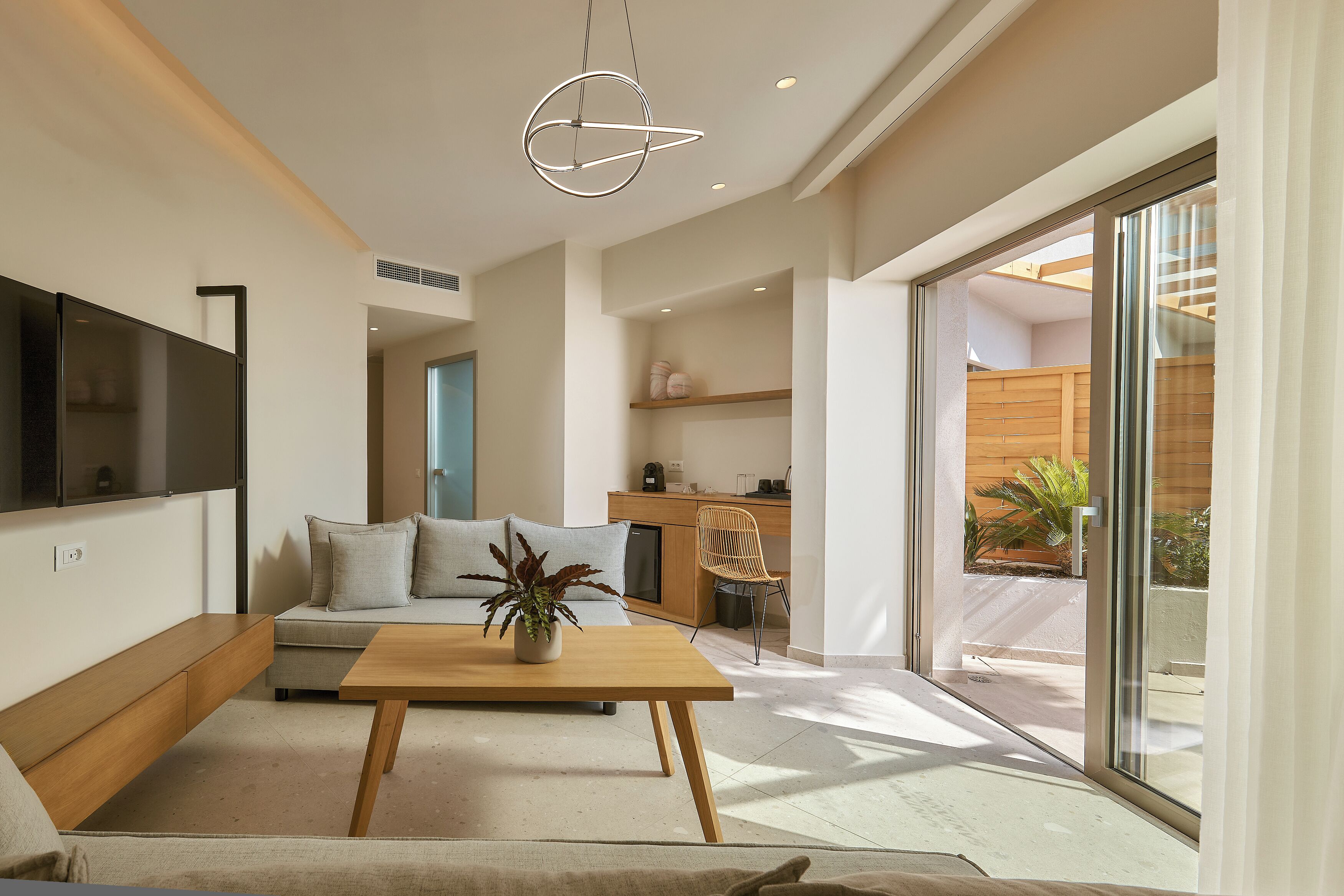 Una sala de estar moderna con sofá, una mesa de centro y un televisor. Hay una puerta corrediza de vidrio que da a un área exterior.