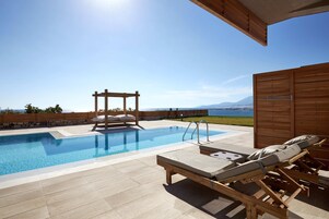 Zona de piscina con sillas de descanso y una pérgola, con vistas a un paisaje pintoresco.