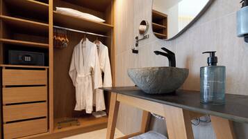 Ein modernes Badezimmer mit einem großen Steinsink, einem Spiegel, einer Holzwaschkommode und einem begehbaren Kleiderschrank mit aufgehängten Bademänteln.