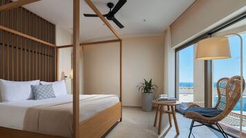 Un dormitorio con cama con dosel, ventilador de techo, planta en maceta, silla de mimbre y vista al océano.