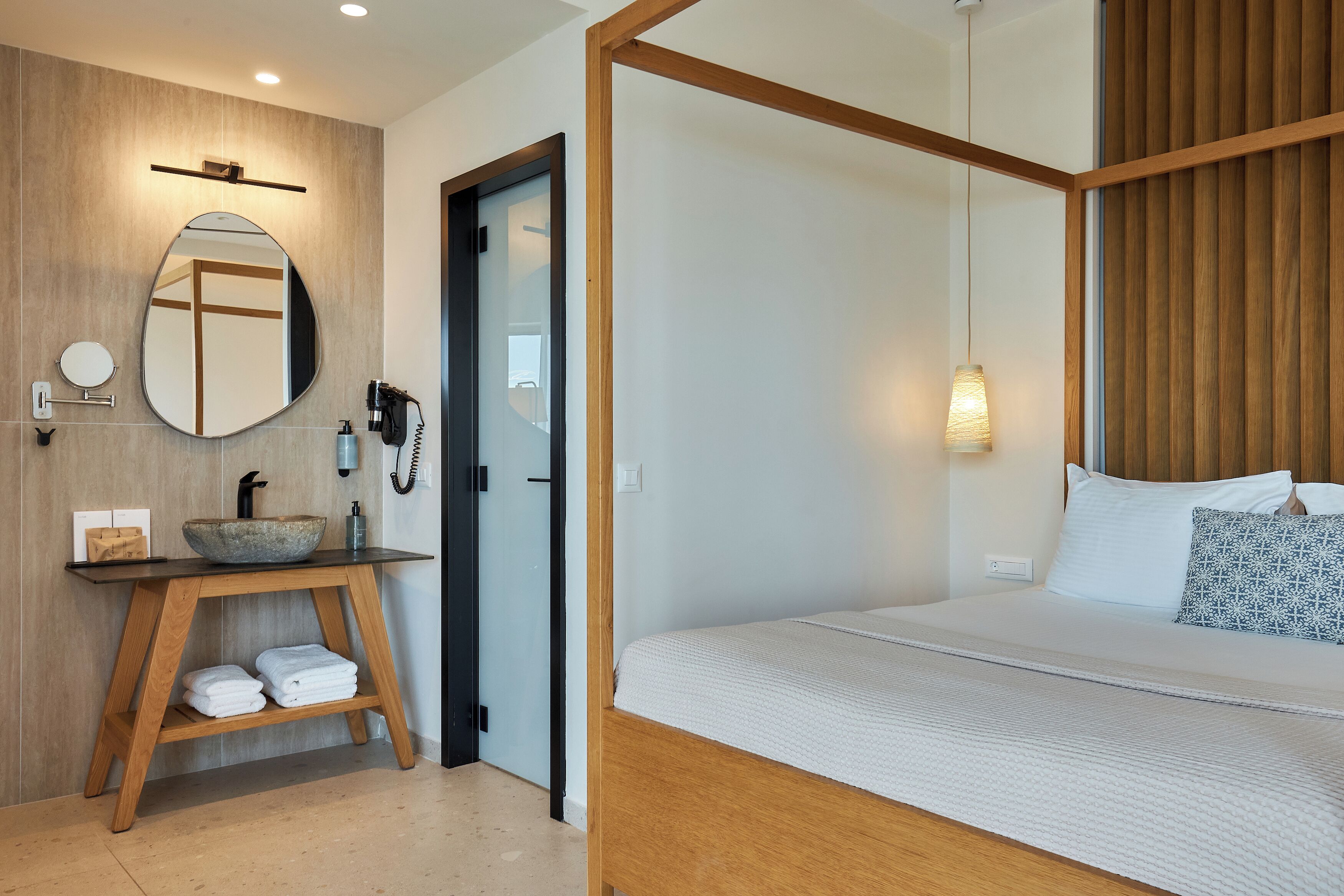 Ein modernes Hotelzimmer mit einem Holznächtigungstisch, einem runden Spiegel, einem Bett mit weißer Bettwäsche und einem Holzkopfstück.