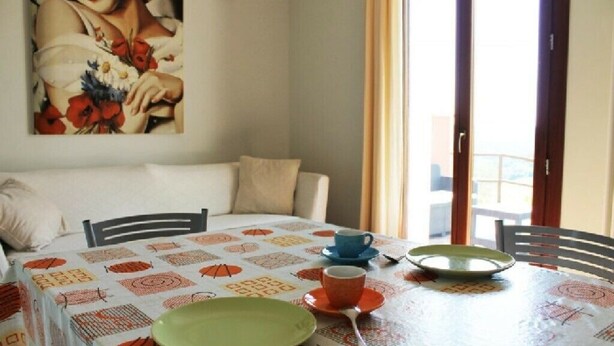 A dining area with a table set for two, a painting on the wall, and a view through the window. - Girasole Apartment on 2 Levels - Renili House (pesaro)