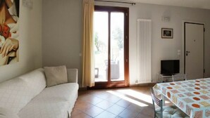 A room with a sofa, a table with a patterned tablecloth, a television, and a sliding glass door leading to an outdoor area. - Girasole Apartment on 2 Levels - Renili House (pesaro)