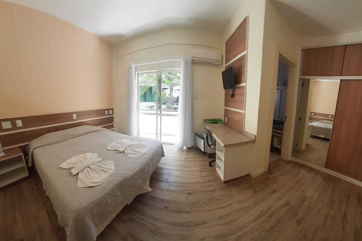 A hotel room with a bed, a desk, a mirror, and a wardrobe.
