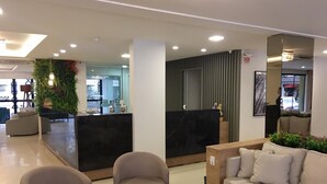 A modern lobby with a reception desk, two armchairs, a sofa, and a small plant.