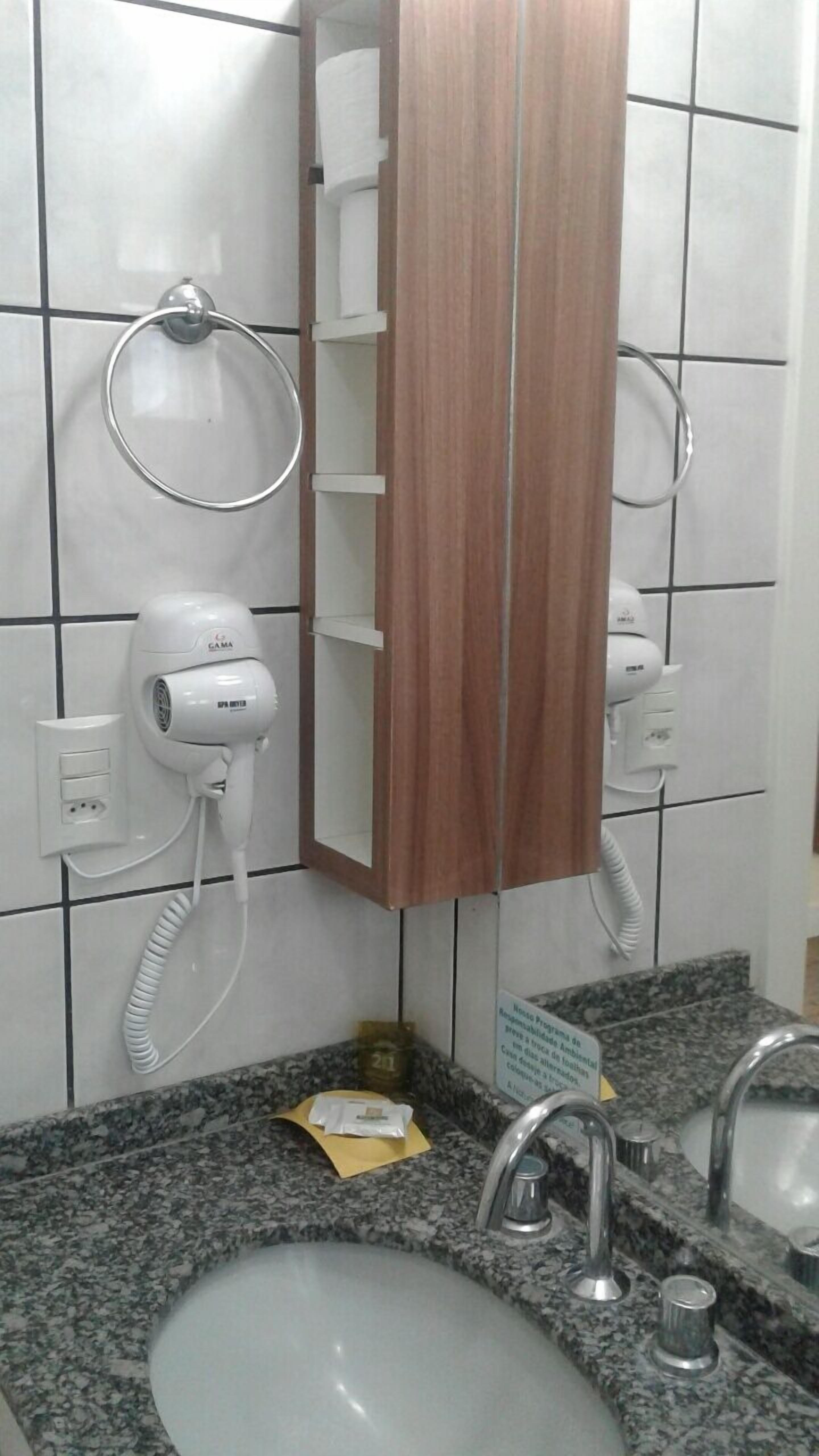A bathroom with a wooden vanity, a white sink, and a hairdryer mounted on the wall.