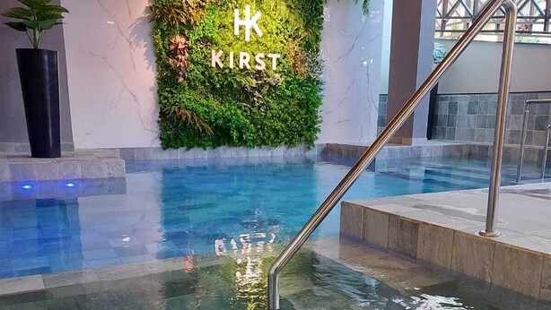 An indoor swimming pool with a glass wall and a green wall with 'KIRST' written on it.