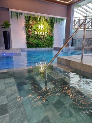 An indoor swimming pool with a glass wall and a green wall with 'KIRST' written on it. - Hotel Kirst (Piratuba)