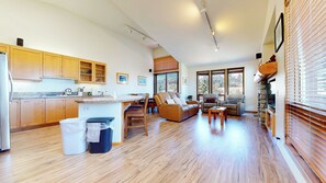 A spacious kitchen with wooden cabinets, a dining area with a table and chairs, a leather sofa, and a stone fireplace. - Pet-Friendly & Stunning Mountain Views, Private Washer/Dryer & 1 Car Garage (Mammoth Lakes)