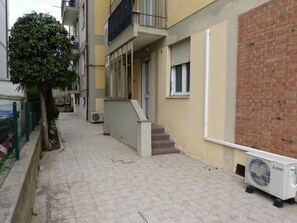 Un estrecho callejón con un edificio a un lado y un árbol al otro. Se ve una escalera que lleva a un nivel superior.