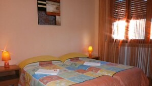 A bedroom with a bed, two bedside lamps, a window with blinds, and a wall-mounted shelf with books. - Airport Pisa Rooms (Pisa)