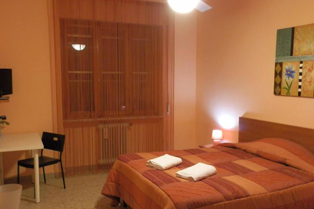 Une chambre à coucher avec un lit, un bureau, une chaise et une fenêtre avec des stores.