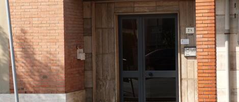 A building entrance with a brick facade, a glass door, and a numbered plaque.