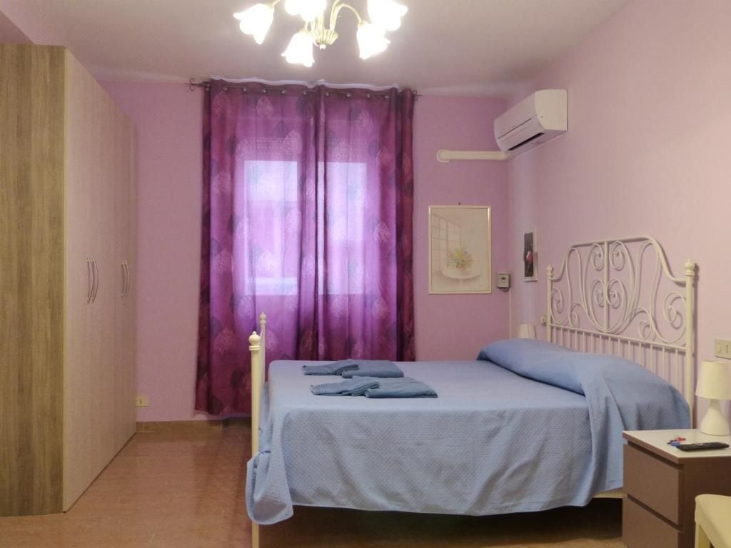 A bedroom with a bed, a nightstand, an air conditioning unit, and a window with purple curtains.