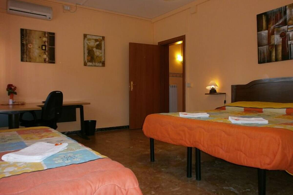 Une chambre d’hôtel avec deux lits, un bureau, une chaise et un tableau au mur.