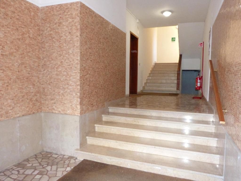 Ein Flur mit einer Treppe, die zu einer oberen Etage führt, einem Feuerlöscher und einer Tür mit einem grünen Notausgangsschild.