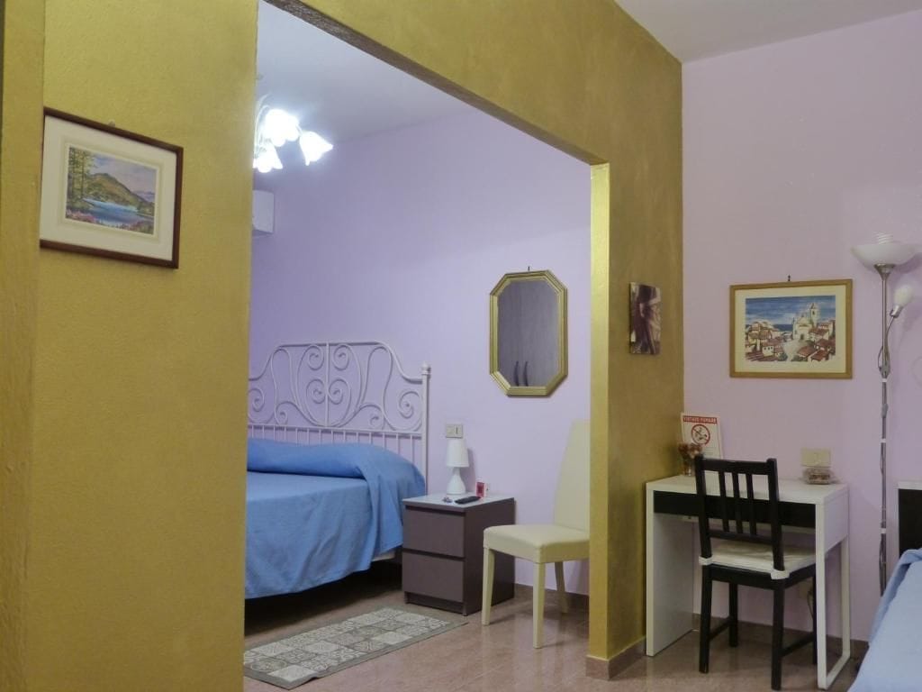 Un dormitorio con cama, mesita de noche, silla, escritorio, lámpara y decoración en la pared.