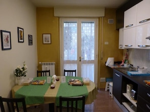Un comedor con una mesa dispuesta para dos, una cocina con armarios blancos y una puerta con paneles de vidrio esmerilado.