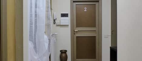 A hallway with a door marked '2', a radiator, a vase, and a white curtain.