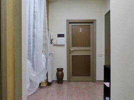 Un corridoio con una porta contrassegnata dal numero 2, un termosifone, un vaso e una tenda bianca.