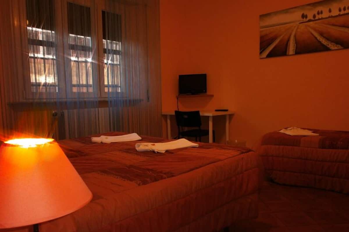 Une chambre d’hôtel avec deux lits, un téléviseur posé sur une petite table et un tableau accroché au mur.