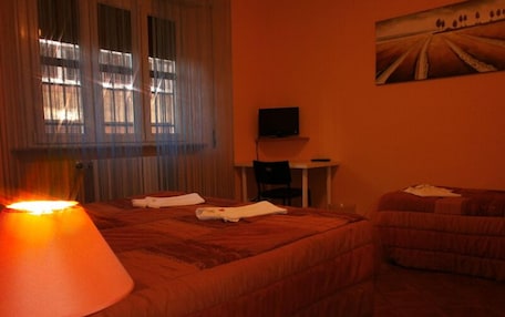 A hotel room with two beds, a TV on a small table, and a painting on the wall.