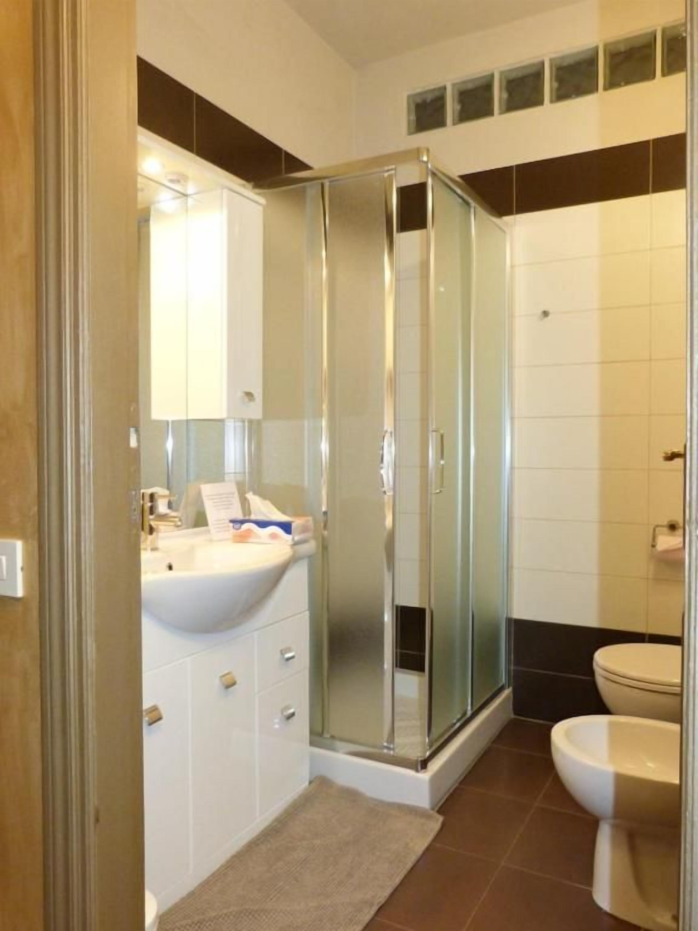 Kylpyhuone, jossa on lasiseinällä varustettu suihku, peilillä varustettu pesuallas ja wc.