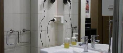 Un baño con lavamanos blanco, espejo y secador de pelo.
