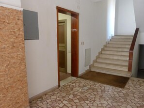 A hallway with a tiled floor, a wooden door, and a staircase with a wooden handrail. - Airport Pisa Rooms (Pisa)