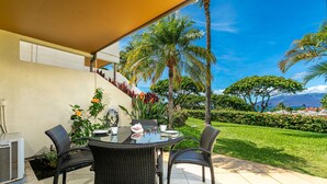 Un patio con una mesa redonda y sillas, rodeado de plantas en macetas y vistas a un exuberante jardín y montañas.