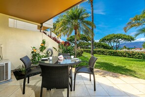 Un patio con un tavolo rotondo e sedie, circondato da piante in vaso e vista su un giardino rigoglioso e montagne.