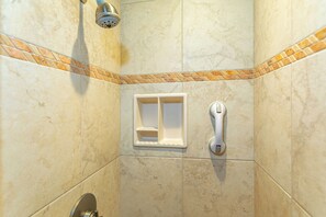 A shower with a handheld showerhead, a soap dish, and a wall-mounted control.