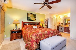 A bedroom with a large bed, a nightstand, a desk, and a ceiling fan.