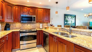 Una cocina moderna con armarios de madera, encimeras de granito, electrodomésticos de acero inoxidable e iluminación colgante.